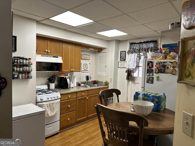 2195 Wilson Rd NW, Conyers, GA 30012 - kitchen with white gas stove, under cabinet range hood, brown cabinetry, light wood-type flooring, and a paneled ceiling