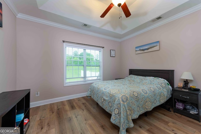 bedroom with wood finished floors, crown molding, baseboards, ceiling fan, and a tray ceiling