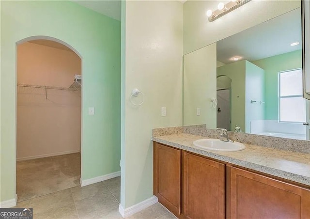 bathroom featuring a walk in closet, a stall shower, vanity, and baseboards