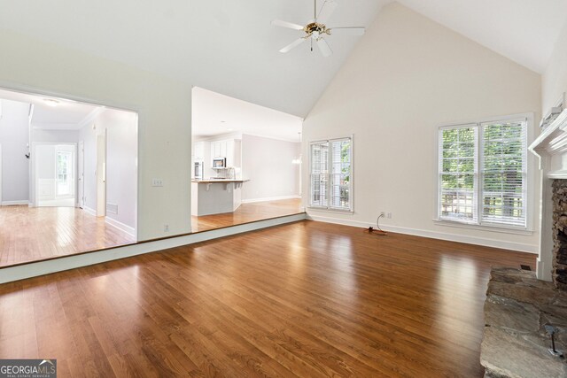 936 Bramble Oak Ct, Powder Springs, GA 30127 - unfurnished living room featuring a stone fireplace, high vaulted ceiling, a ceiling fan, wood finished floors, and healthy amount of natural light