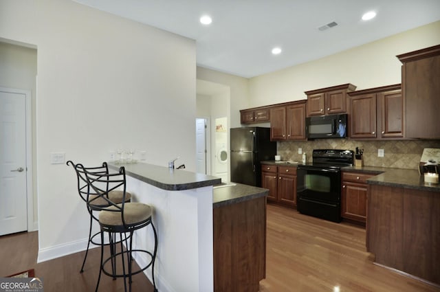 2595 Grapevine Cir, Cumming, GA 30041 - kitchen with black appliances, dark countertops, a peninsula, a breakfast bar area, and dark wood-type flooring