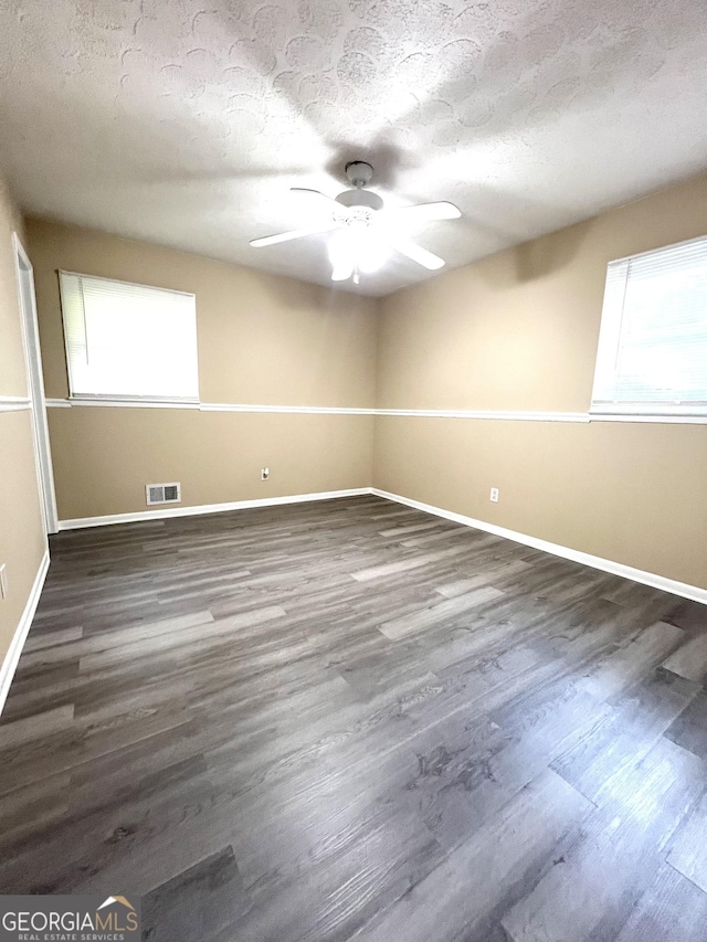unfurnished room with healthy amount of natural light, a ceiling fan, wood finished floors, baseboards, and a textured ceiling
