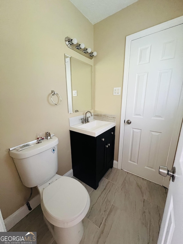 bathroom featuring vanity, toilet, baseboards, and marble look tile flooring