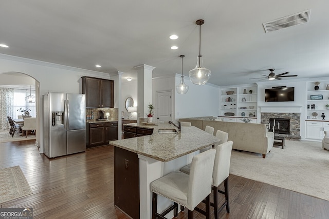 kitchen featuring stainless steel refrigerator with ice dispenser, a ceiling fan, ornamental molding, a kitchen bar, and light stone countertops