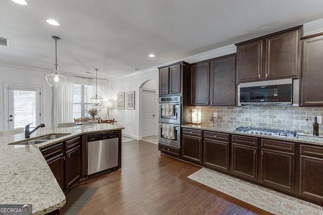 kitchen with appliances with stainless steel finishes, a sink, crown molding, dark brown cabinets, and light stone countertops