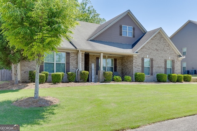 view of front of house featuring a front yard, brick siding, central AC, and roof with shingles