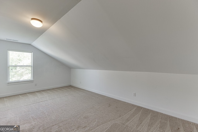additional living space featuring light colored carpet, lofted ceiling, and baseboards