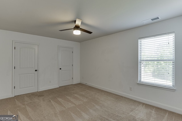unfurnished bedroom featuring light carpet, two closets, baseboards, and a ceiling fan