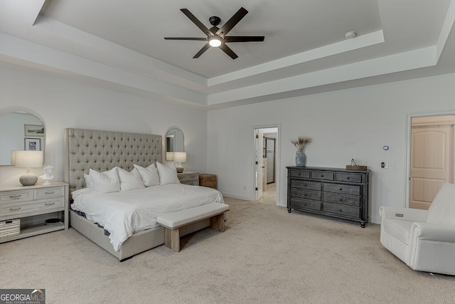bedroom with a tray ceiling, light colored carpet, baseboards, and a ceiling fan