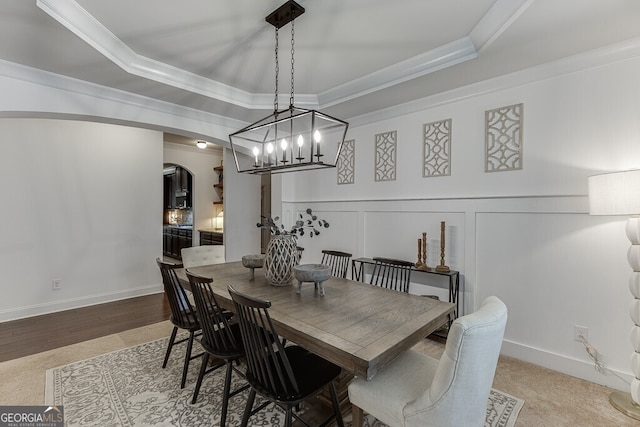 dining space with arched walkways, a tray ceiling, ornamental molding, a decorative wall, and a wainscoted wall