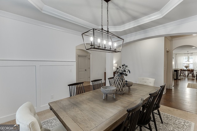 dining area featuring arched walkways, ornamental molding, a chandelier, a decorative wall, and wood finished floors