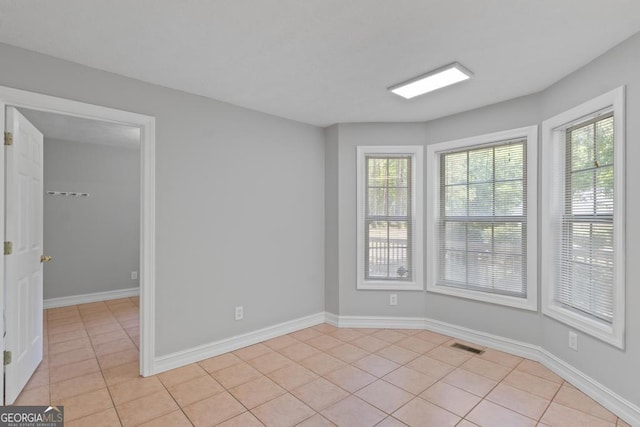 empty room with light tile patterned floors, plenty of natural light, and baseboards