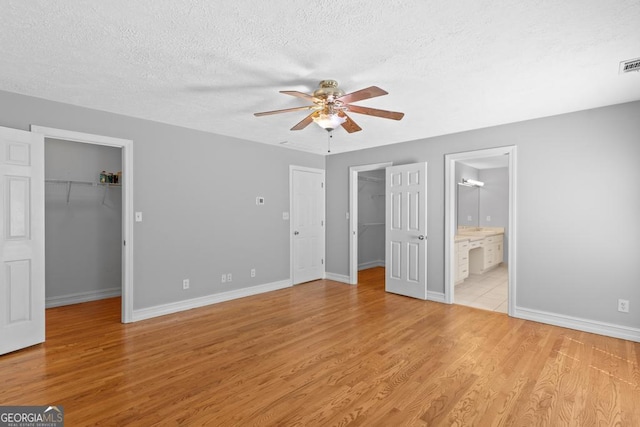 unfurnished bedroom featuring a walk in closet, a closet, a textured ceiling, light wood finished floors, and baseboards