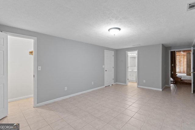 unfurnished bedroom with a textured ceiling, baseboards, light tile patterned flooring, and connected bathroom