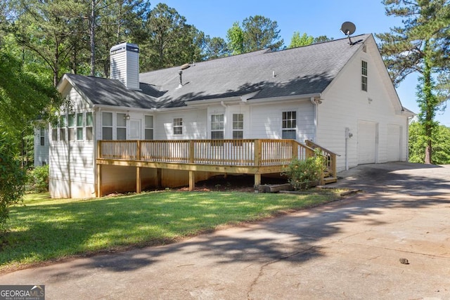 back of property featuring a deck, an attached garage, a chimney, concrete driveway, and a yard