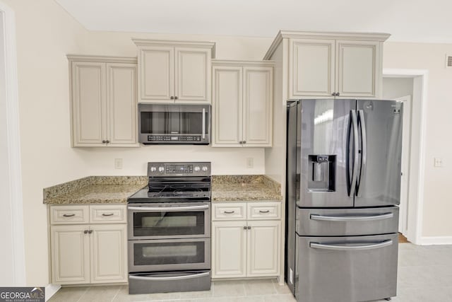 kitchen with appliances with stainless steel finishes, cream cabinets, light stone countertops, and light tile patterned flooring