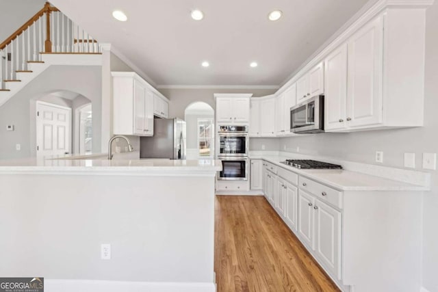 5034 Hickory Hills Dr, Woodstock, GA 30188 - kitchen featuring appliances with stainless steel finishes, arched walkways, light wood-style floors, a peninsula, and white cabinetry