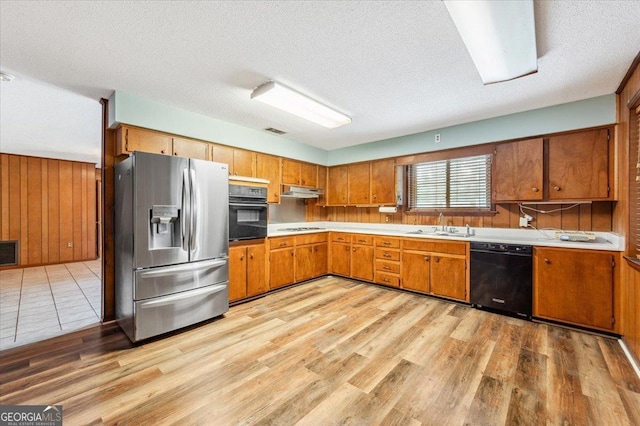 kitchen with black appliances, brown cabinets, light countertops, a textured ceiling, and wooden walls