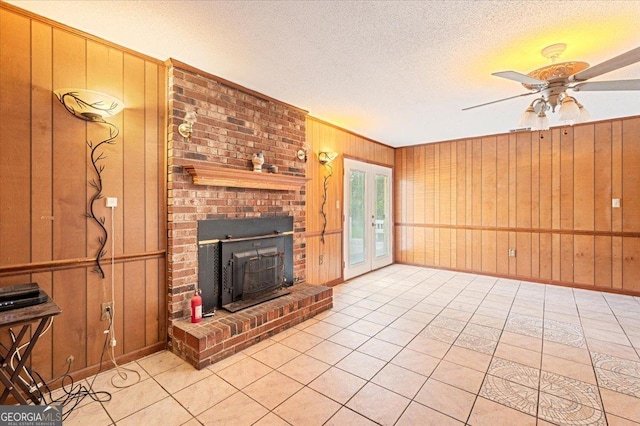 unfurnished living room with wood walls, a textured ceiling, a ceiling fan, light tile patterned floors, and baseboards