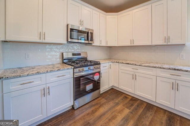 kitchen with stainless steel appliances, white cabinetry, tasteful backsplash, dark wood-type flooring, and light stone countertops
