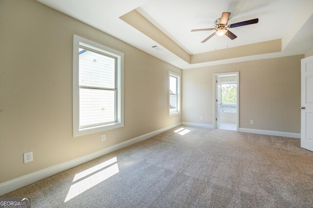 carpeted empty room featuring a ceiling fan, a tray ceiling, and baseboards