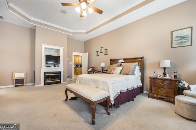bedroom featuring a raised ceiling, light carpet, crown molding, a glass covered fireplace, and baseboards