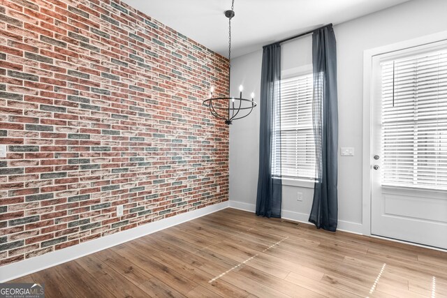 4462 Dandelion Ln, Atlanta, GA 30342 - unfurnished dining area with brick wall, baseboards, a chandelier, and light wood-style floors