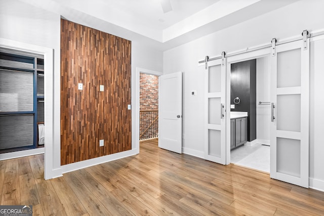 4462 Dandelion Ln, Atlanta, GA 30342 - unfurnished bedroom with a barn door, light wood-type flooring, and connected bathroom