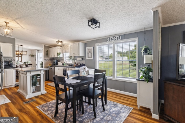 dining area with dark wood-style flooring, a textured ceiling, a chandelier, ornamental molding, and baseboards