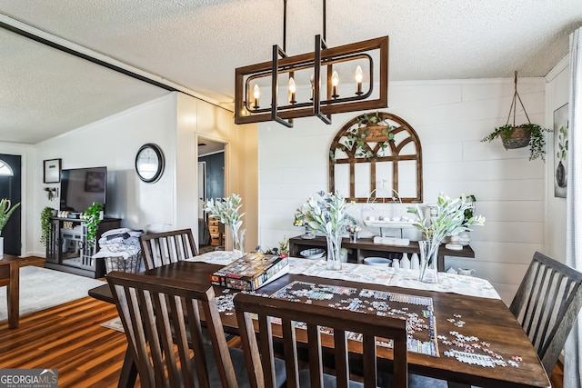 dining space with a textured ceiling, wood finished floors, a chandelier, and ornamental molding