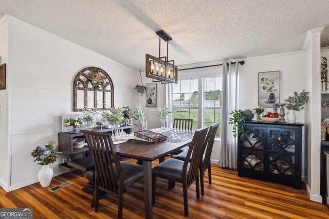 dining space featuring a chandelier, a textured ceiling, wood finished floors, lofted ceiling, and crown molding