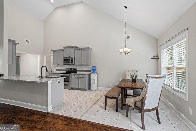kitchen featuring stainless steel appliances, gray cabinetry, a sink, high vaulted ceiling, and light stone countertops