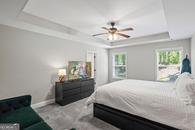carpeted bedroom featuring a raised ceiling, multiple windows, baseboards, and a ceiling fan