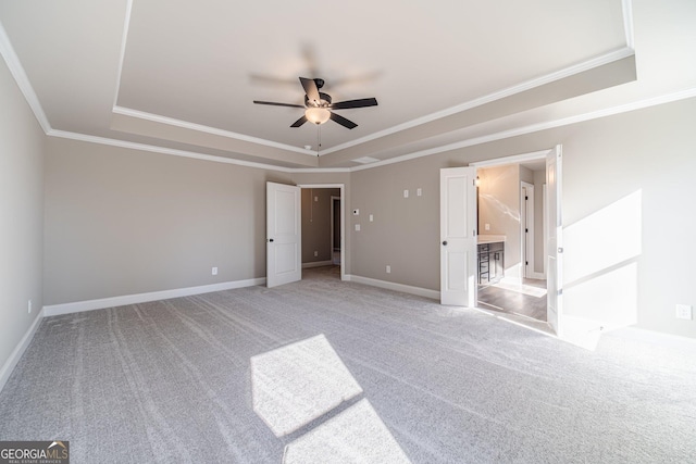 unfurnished bedroom featuring a raised ceiling, light carpet, ornamental molding, baseboards, and ceiling fan