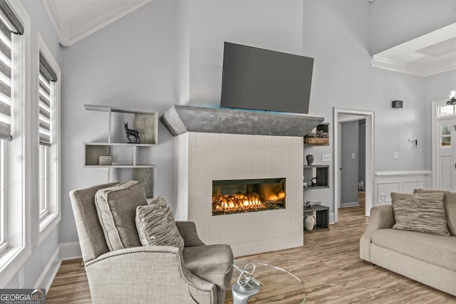 living area featuring crown molding, a lit fireplace, wood finished floors, and a towering ceiling