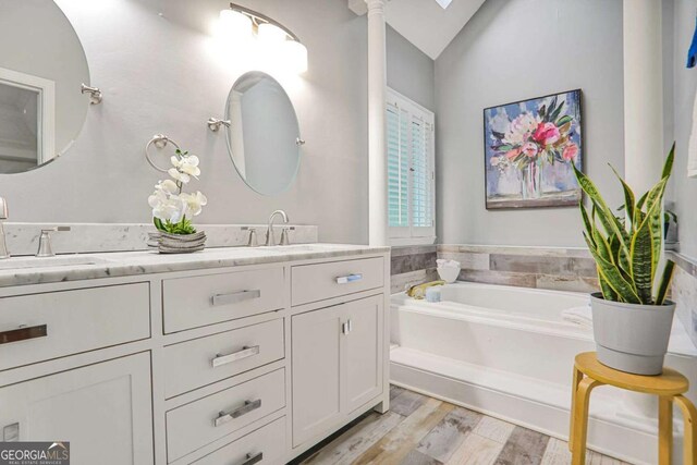 bathroom featuring wood finished floors, double vanity, lofted ceiling, and a garden tub