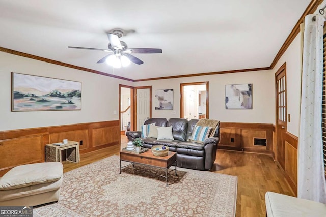 living room featuring wainscoting, wood finished floors, a ceiling fan, and crown molding