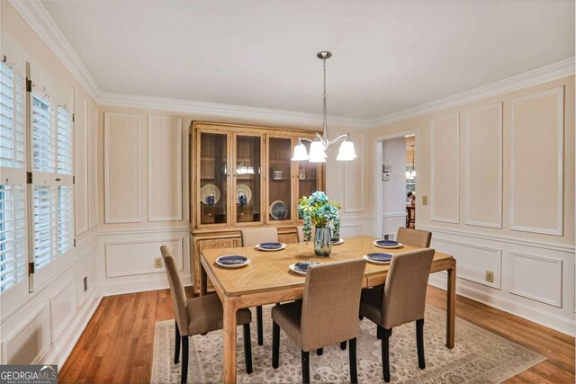 dining room featuring a decorative wall, a chandelier, light wood-type flooring, and crown molding