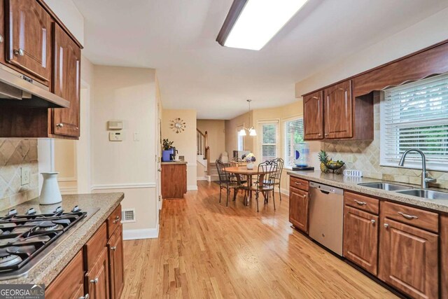 kitchen with stainless steel appliances, a sink, light wood-style flooring, tasteful backsplash, and hanging light fixtures
