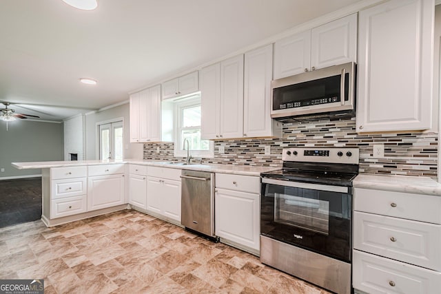 kitchen with stainless steel appliances, a sink, light countertops, a peninsula, and white cabinetry