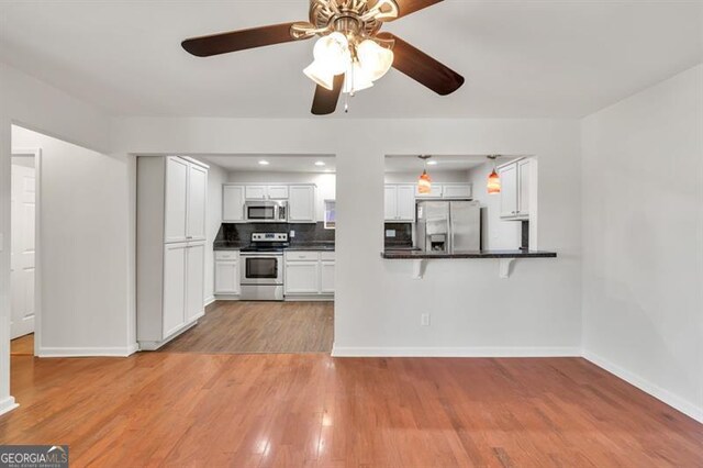 kitchen with appliances with stainless steel finishes, ceiling fan, dark countertops, light wood-type flooring, and white cabinetry