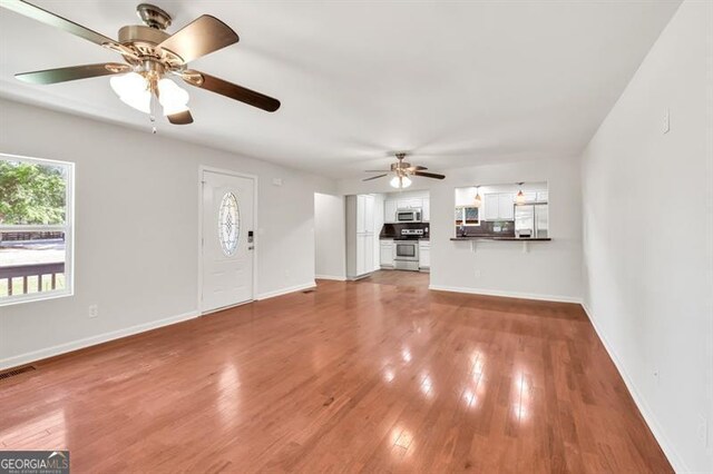 unfurnished living room featuring a ceiling fan, light wood-style floors, and baseboards