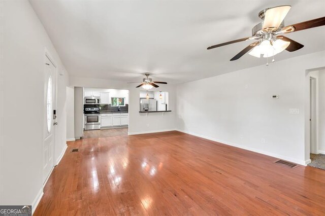 unfurnished living room with a ceiling fan, wood finished floors, and baseboards