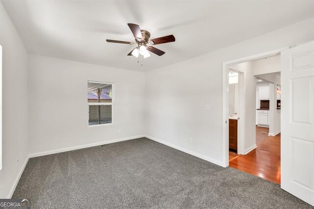 spare room featuring dark colored carpet, ceiling fan, and baseboards