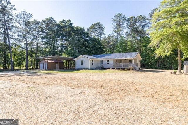 view of front of house with covered porch, an outbuilding, dirt driveway, a carport, and view of wooded area