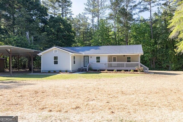 ranch-style home with covered porch, a detached carport, metal roof, and a front lawn