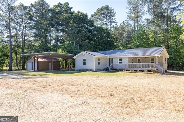 view of front of property featuring covered porch, an outbuilding, a detached carport, driveway, and view of wooded area