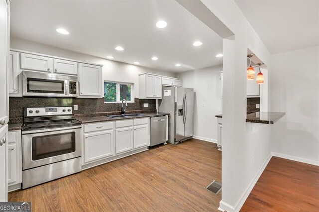 kitchen featuring appliances with stainless steel finishes, a sink, wood finished floors, backsplash, and baseboards