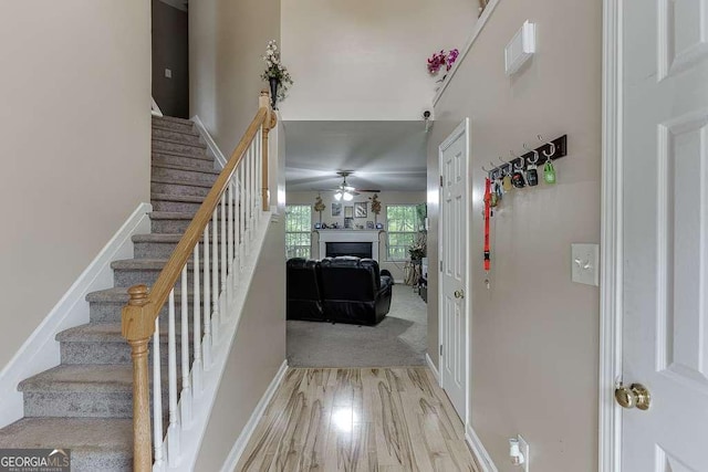 staircase featuring a fireplace, a ceiling fan, wood finished floors, and baseboards