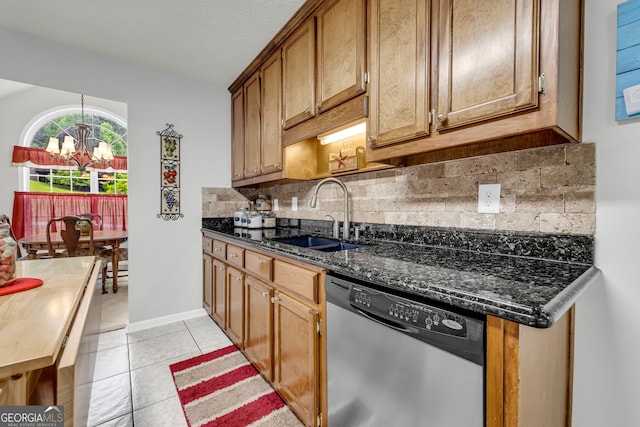 kitchen with dishwasher, a sink, a chandelier, light tile patterned flooring, and dark stone countertops